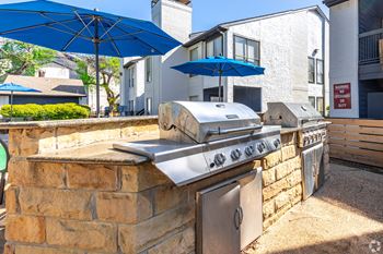 A blue umbrella is above a grill on a stone wall.